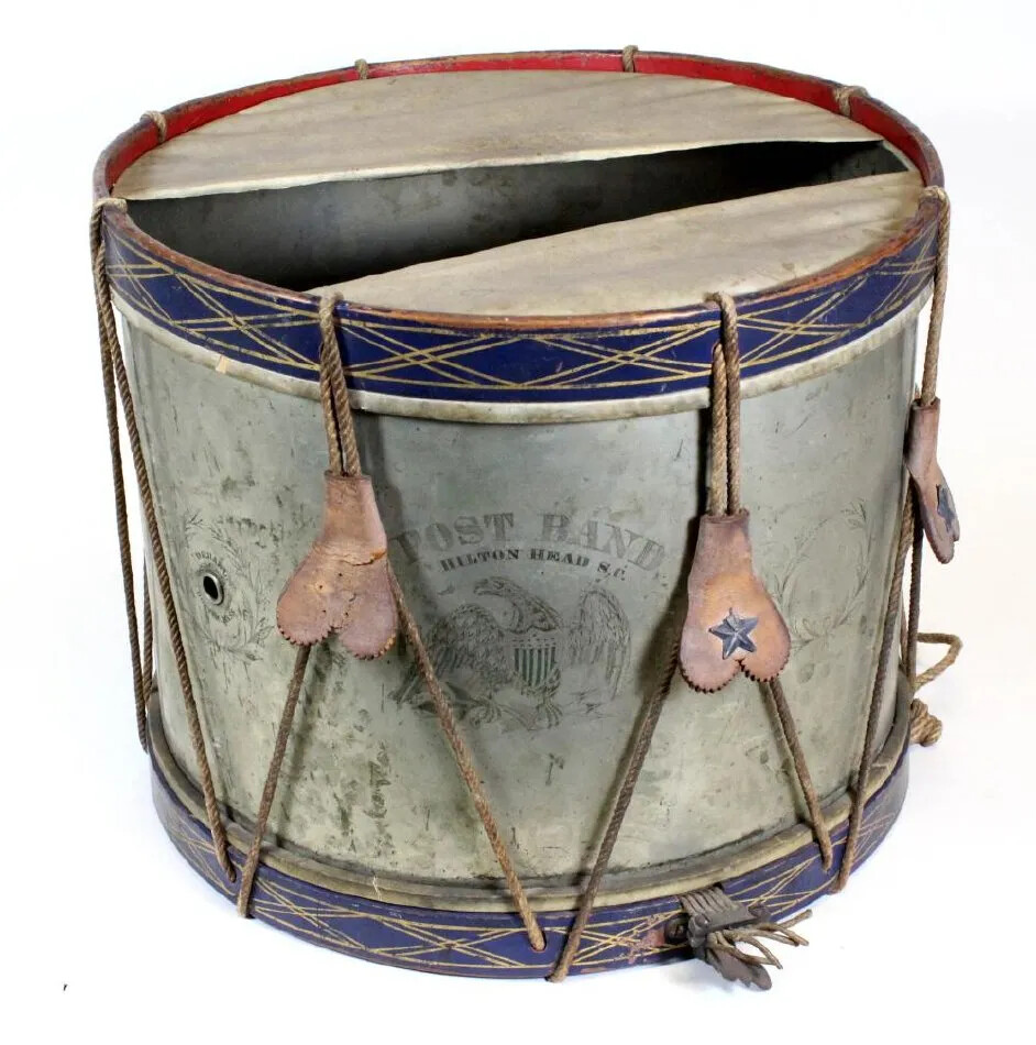 A drum is 13.5 inches high and 17 inches in diameter. The sides are nickel-plated brass engraved with seven broken wreaths. In the center of the wreaths is an eagle with outspread wings and shield; it has lettering above. The lettering reads "POST BAND. / HILTON HEAD S.C." There is a maker's mark reading "D.C. HALL. / MANUFACTURER, / BOSTON, MASS." around a  vent hole on one side. On the top and bottom of the drum, there are wooden bands painted dark blue with gilt decorations keeping the parchment heads taught. The top parchment head is torn down the middle. 