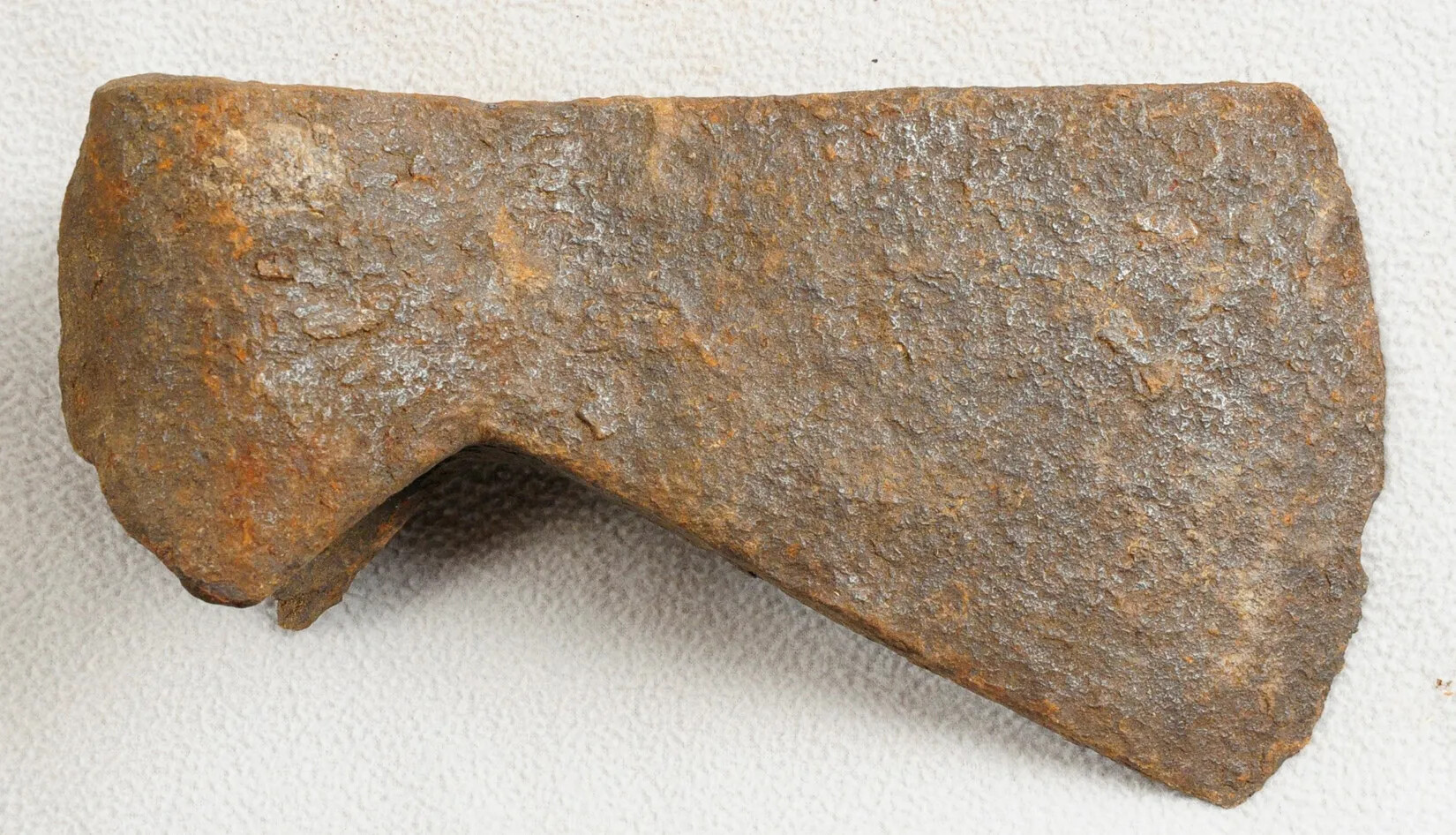 A rusty metal ax head, with a rounded edge on one side and a sharp flattened edge on the other. 