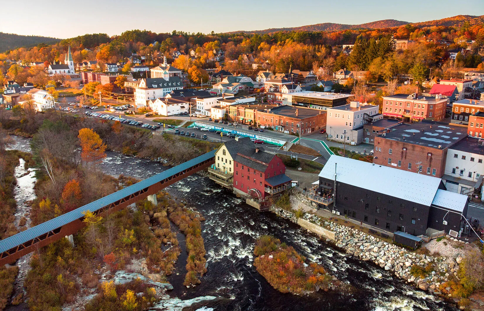 A colored photograph of a town situated on the banks of a river. There is a large covered bridge that connects the town to the other side of the river.