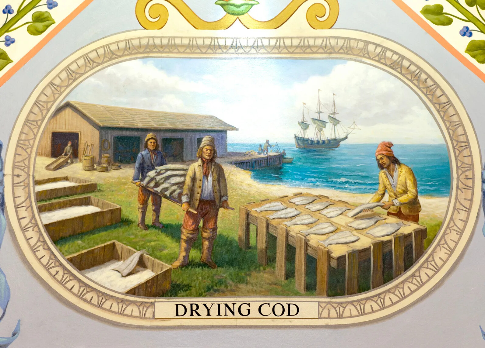 A colored painting of a group of men in fishermen's outfits. All of the men are engaged in different activities, like lying filleted fish bodies on wide wooden racks, carrying a pile of filleted fish, salting the fish, or helping each other out of a rowboat. In the distance is a large ship with three tall masts and sails. The title of the painting, located centered along the bottom border, reads "DRYING COD."