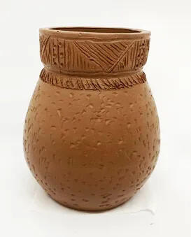 A brown clay pot. The base and rim of the pot are decorated with  carved geometric patterns.
