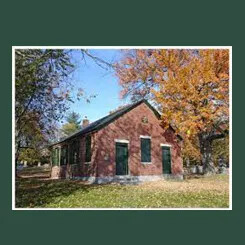 Brick schoolhouse surrounded by autumn trees under a clear blue sky.