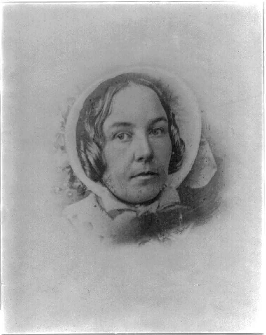 An old black and white photograph shows a woman's head in a bonnet. She is looking to the left and her dark hair comes out from the side of the bonnet next to her face. 