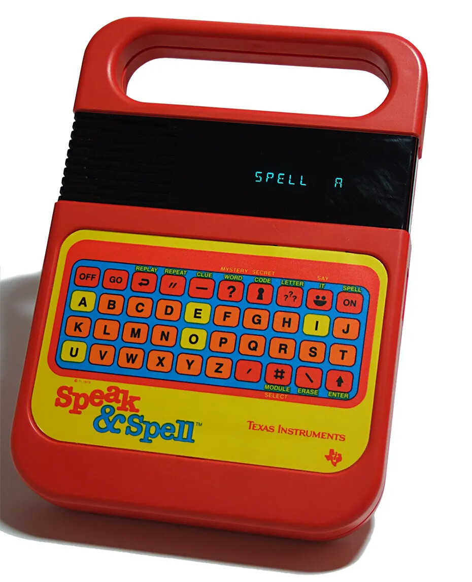 Red rectangular plastic object with rounded corners and a handle. A black screen has blue text SPELL/A. Standard touchscreen keyboard. Text SPEAK/AND/SPELL on lower left. Text TEXAS/INSTRUMENTS and Texas Instruments logo on lower right.