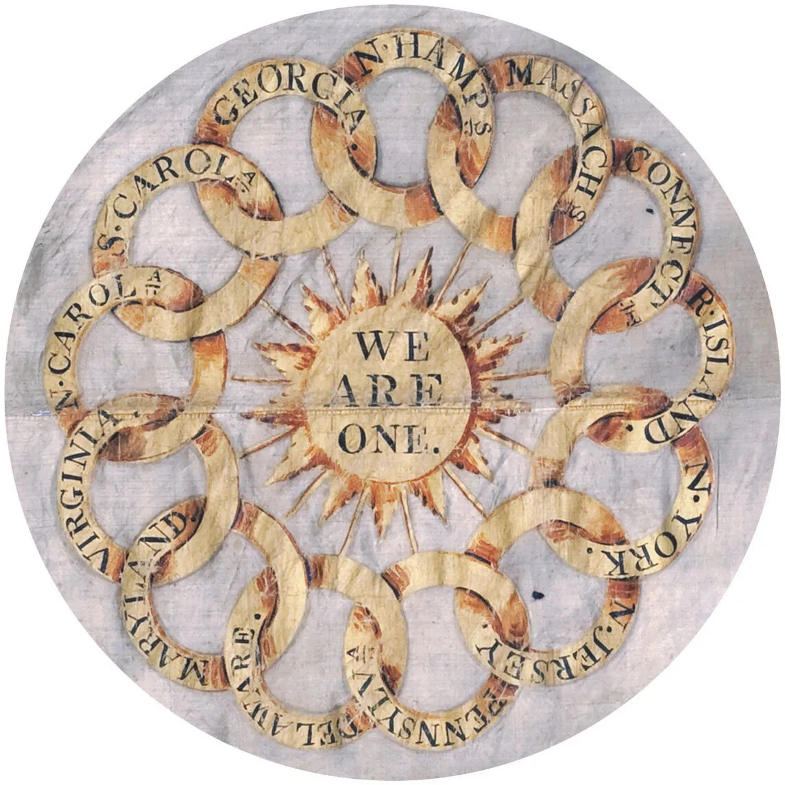 Close up of center image in a flag. A set of thirteen rings with the names of the original thirteen colonies interlace. From clockwise top, they read “N.HAMPS/MASSACHS/CONNECT/R.ISLAND/N.YORK./N.JERSEY/PENNSYLVA/DELAWARE./MARYLAND./N.CAROLA/S.CAROLA/GEORGIA.” In the center of the rings is a sun with the words “WE/ARE/ONE.” To the left of the rings are three misshaped holes in a vertical line.