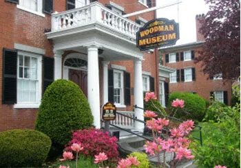 Entrance of Woodman Museum with brick building, garden, and sign.