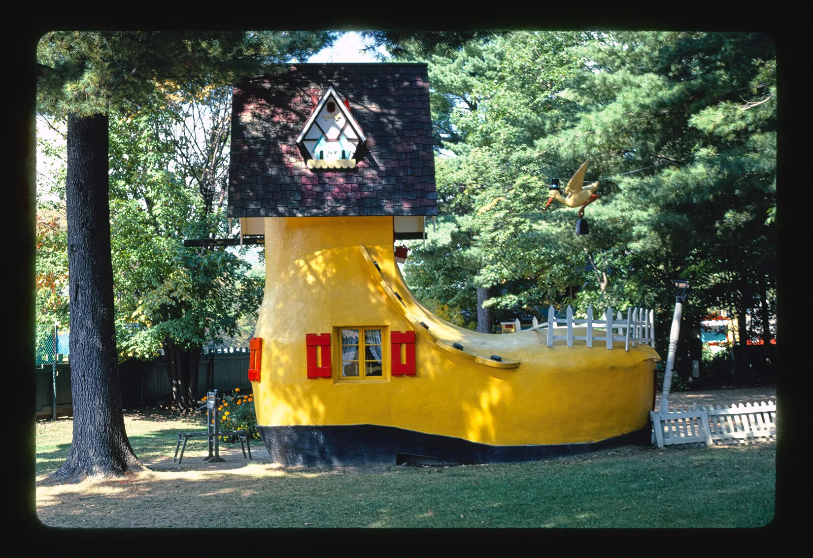 A giant yellow boot has been made into a home. A yellow bird wearing a top hat flies toward the shoe home carrying a briefcase. 