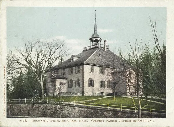A colored postcard of a multi-storied building with a tall steeple. The building rests on a hill of green grass, surrounded by a white picket fence and leafless trees. The title of the postcard, located along the bottom border, reads "7108, HINGHAM CHURCH, HINGHAM, MASS, (OLDEST PARISH CHURCH IN AMERICA.)."