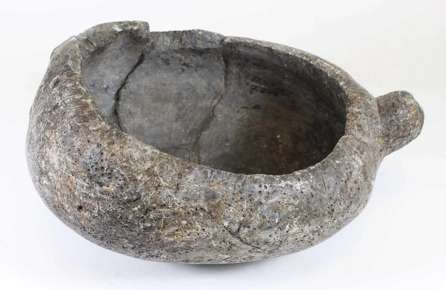 A large, gray stone bowl with a small stone handle which juts out on the right-hand side. The inside of the bowl is slightly cracked.
