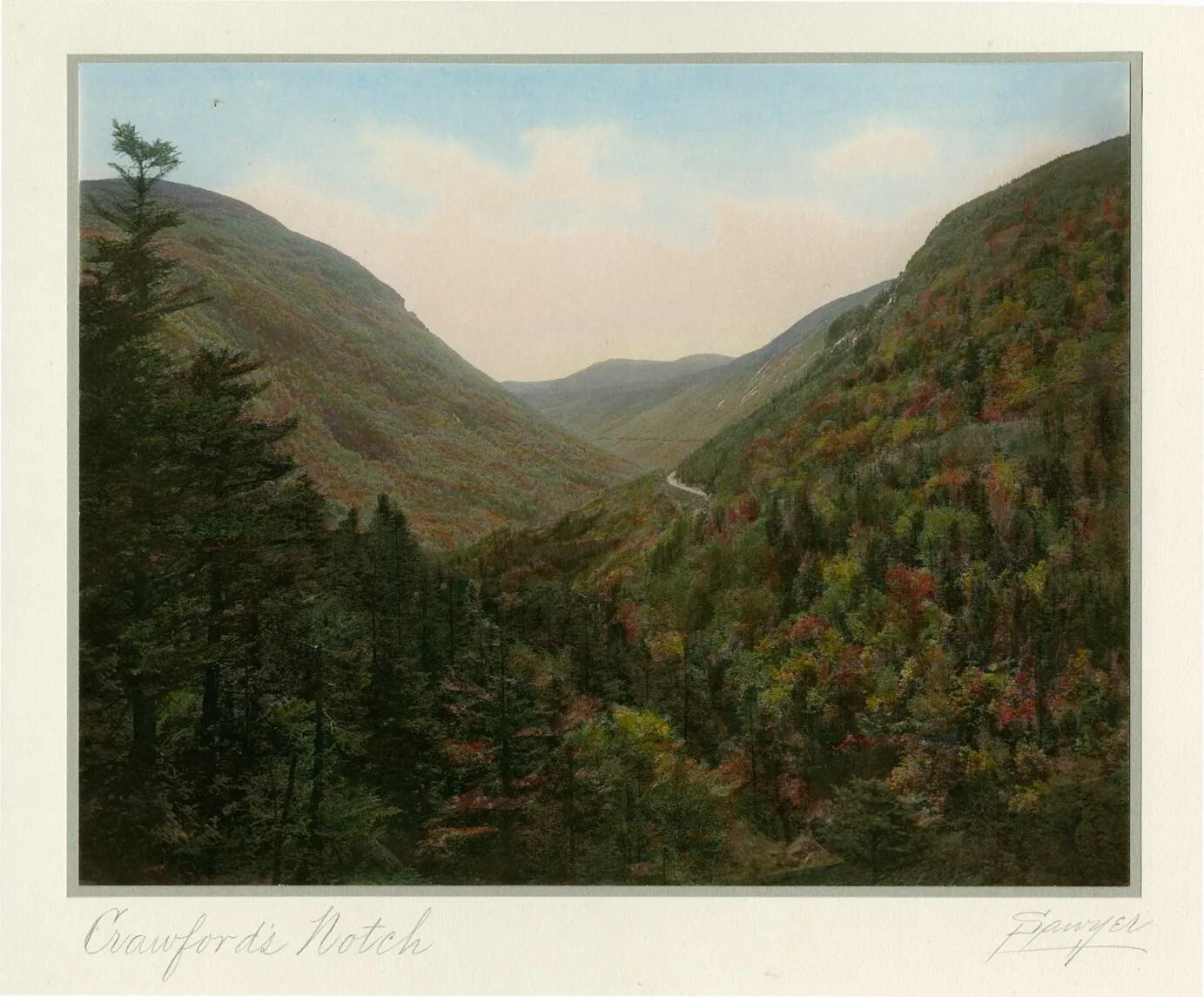 A colored postcard of a mountain region. Green trees are mixed in with multi-colored trees in the valley of the mountains. Above the mountain region is a clouded blue sky.